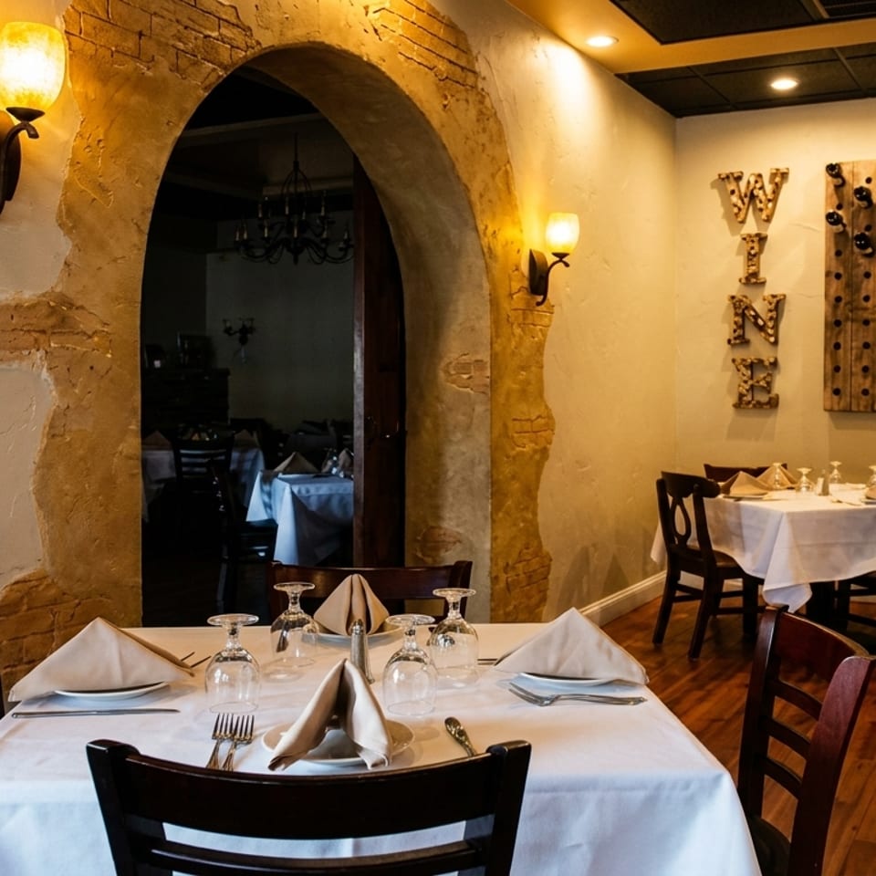 Restaurant interior with set tables, an arched doorway, and a "WINE" sign with a wine rack.