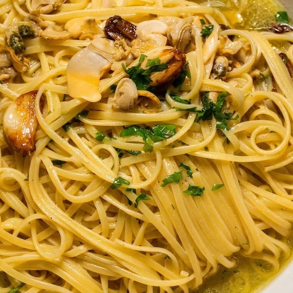 Close-up of linguine pasta with clams, garlic, and parsley in a white bowl.