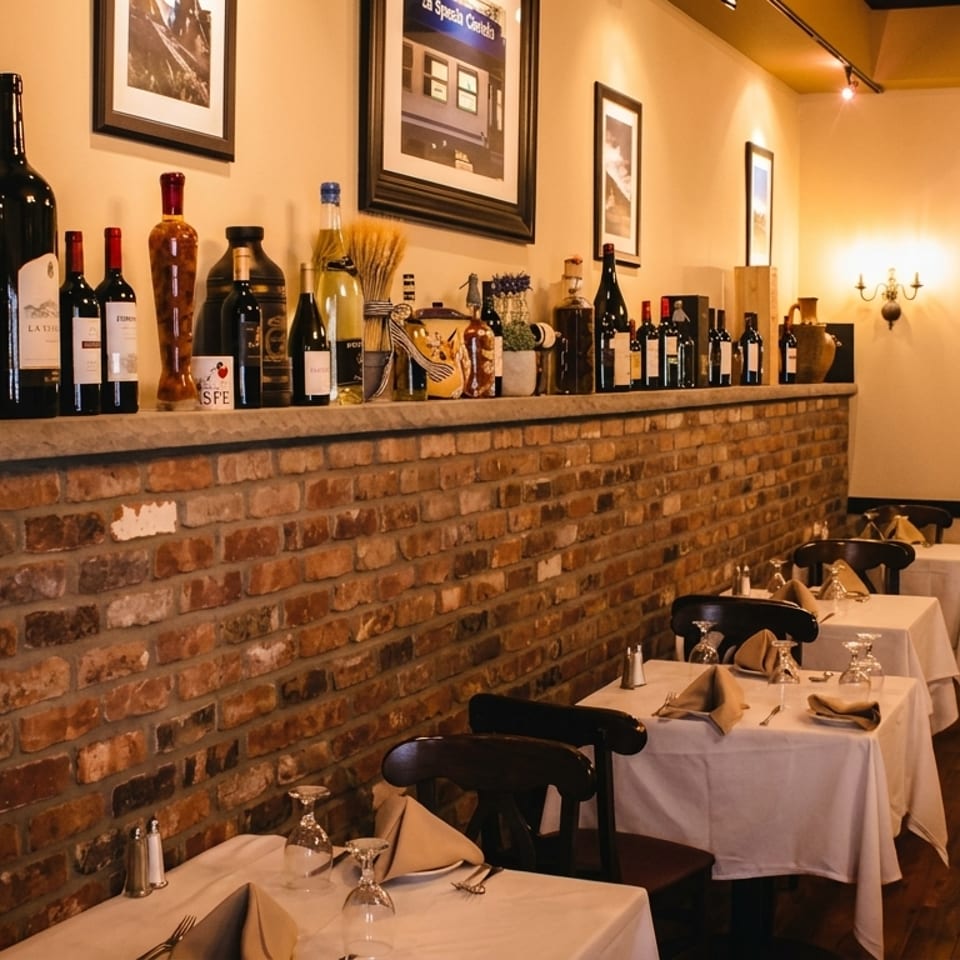 Cozy Italian restaurant interior with brick walls, wine bottles on a shelf, and set tables.