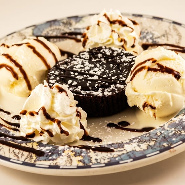Chocolate lava cake with powdered sugar, vanilla ice cream, whipped cream, and chocolate syrup on a plate.